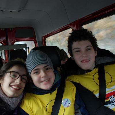 Marija, Christopher und Julian sitzen auf der Rückbank in Bus und lächeln.