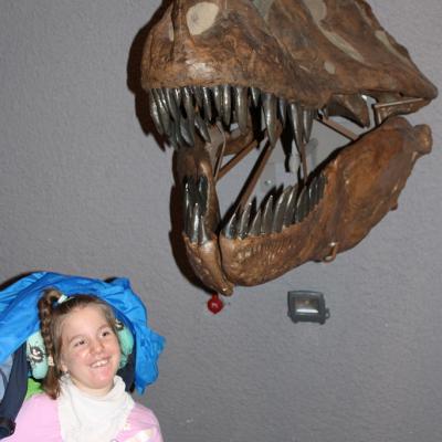 Eine Schülerin im Rollstuhl steht unter einem Kopf von einem Dinosaurier.