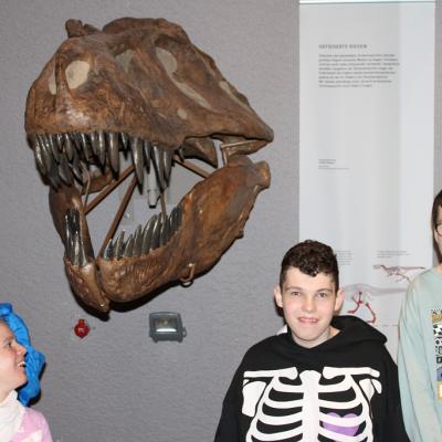 Drei Schüler stehen unter einem Dinosaurier Kopf 
