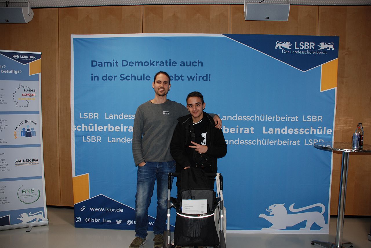 Herr Kling und Aziz stehen vor einer blauen Wand des LSK.