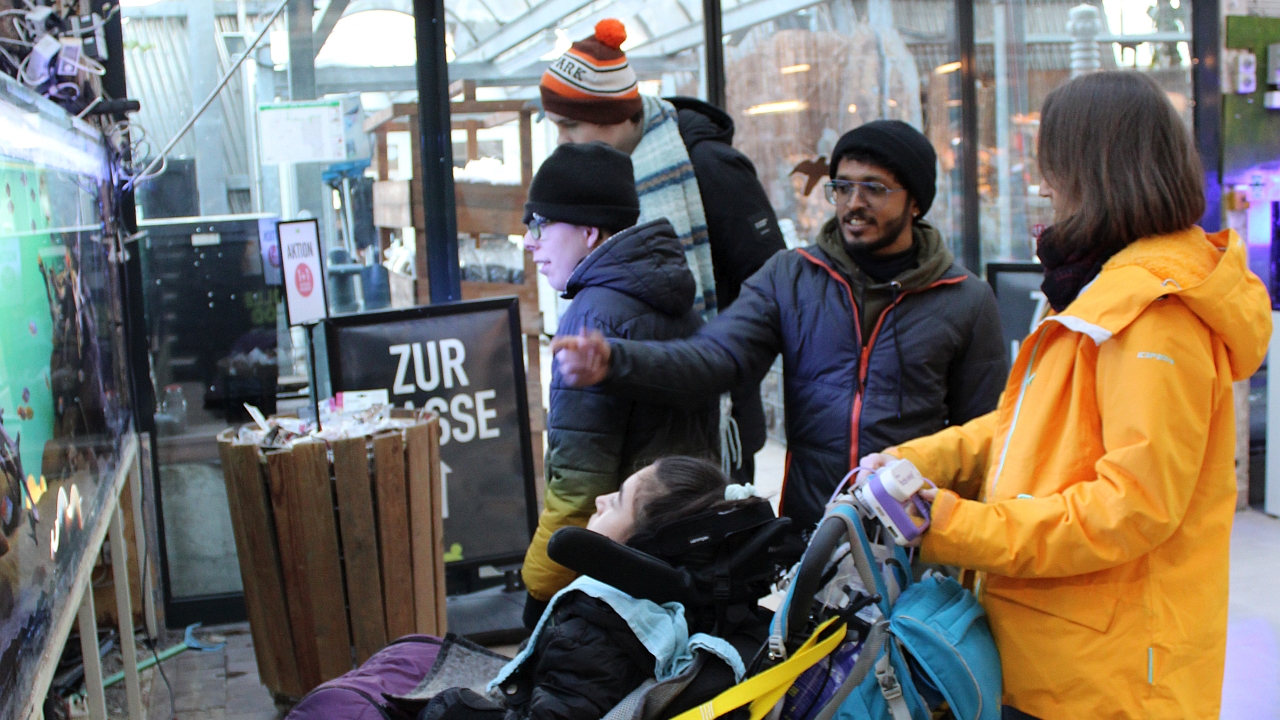 Eine Rollstuhlfahrern, zwei Schüler, eine Betreuerin und ein BFD schauen sich das Aquarium an und reden über die Fische.