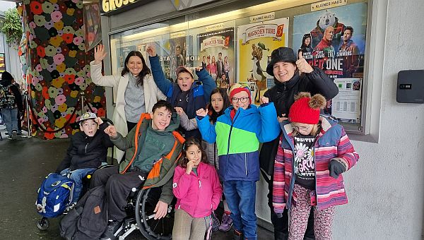 Einige Kinder befinden sich vor einer Kinoplakatwand und freuen sich