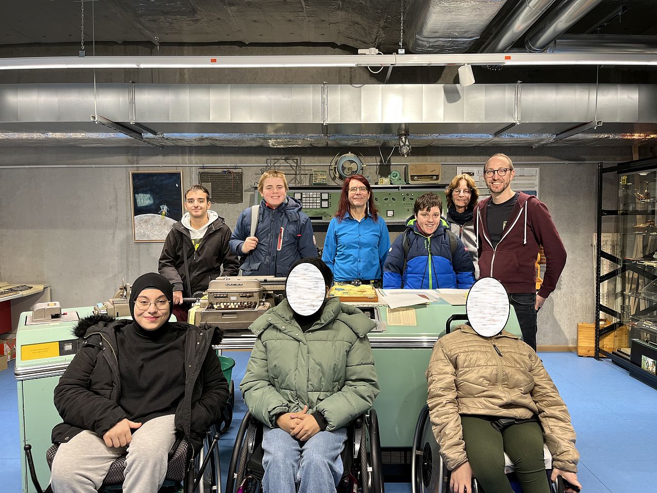 Sechs Schüler: innen, zwei Lehrer: innen und der Museumsmitarbeiter stehen vor und hinter einem großen, alten Computer. Sie lächeln alle in die die Kamera.