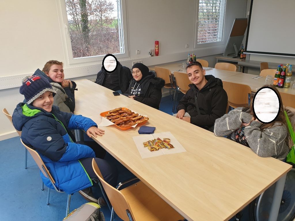 Sechs Schüler: innen sitzen um einen Tisch. Auf dem Tisch stehen Brezeln und Gummibärchen.