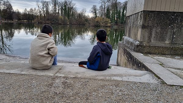 Zwei Jungen sitzen am See und schauen in das Wasser