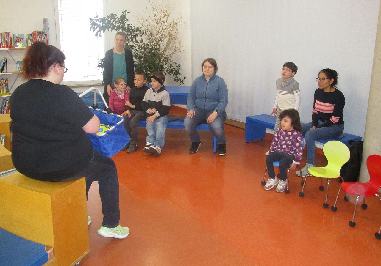 Eine Büchereimitarbeiterin sitzt mit einem Korb im Eingangsbereich der Asperger Bücherei und stellt ihre Medien vor.