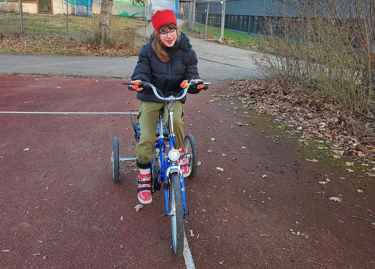Schülerin sitzt auf einem blauen Fahrrad und fährt genau auf der Linie auf dem roten Sportplatz