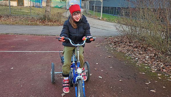 Schülerin sitzt auf einem blauen Fahrrad und fährt genau auf der Linie auf dem roten Sportplatz