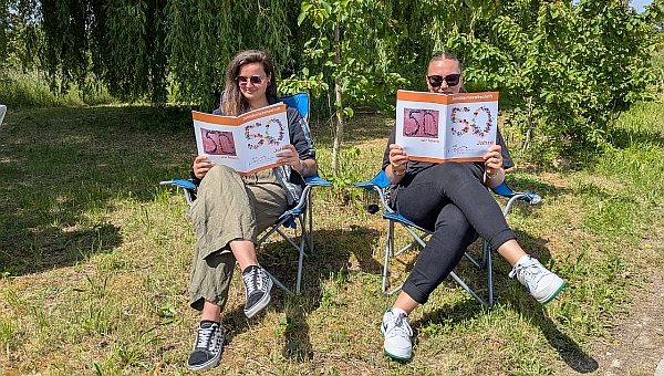 2 Frauen sitzen mit der Festtagszeitung in Campingstühlen und lesen diese durch. 