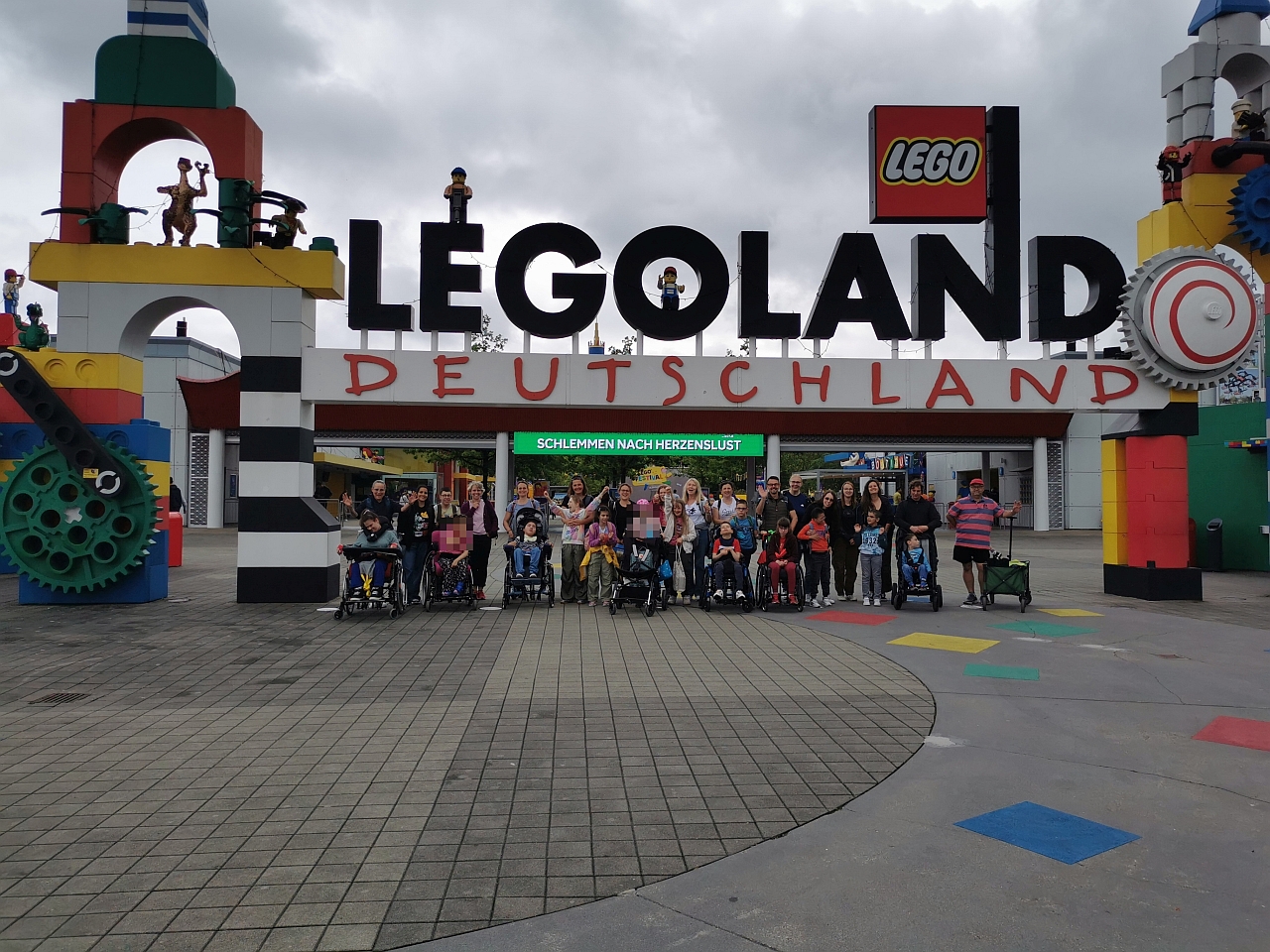Eine große Gruppe von Kindern und Erwachsenen stehen unter einem großen Torbogen aus großen bunten Legosteinen. Ganz oben steht der Schriftzug „Legoland Deutschland“