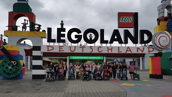 Eine große Gruppe von Kindern und Erwachsenen stehen unter einem großen Torbogen aus großen bunten Legosteinen. Ganz oben steht der Schriftzug „Legoland Deutschland“ 
