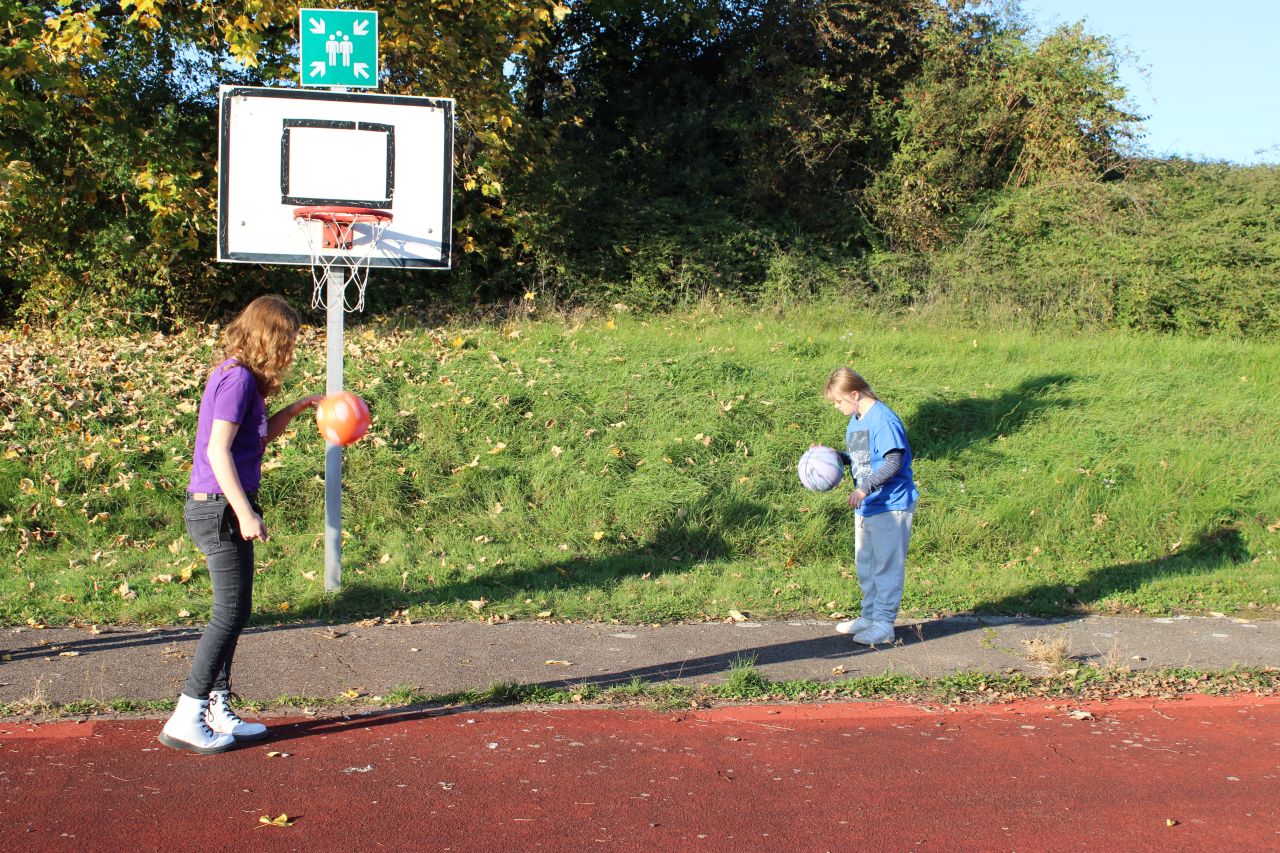Zwei junge Frauen spielen in der Sonne Basketball.