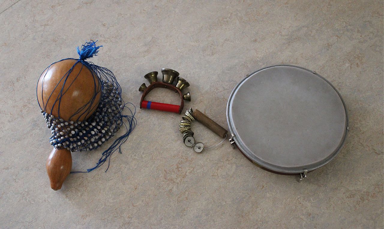 Es sind vier Instrumente zu sehen: Eine Chekere, ein Schellenband, ein selbstgebasteltes Schellenband aus Kronkorken und ein Tamburin