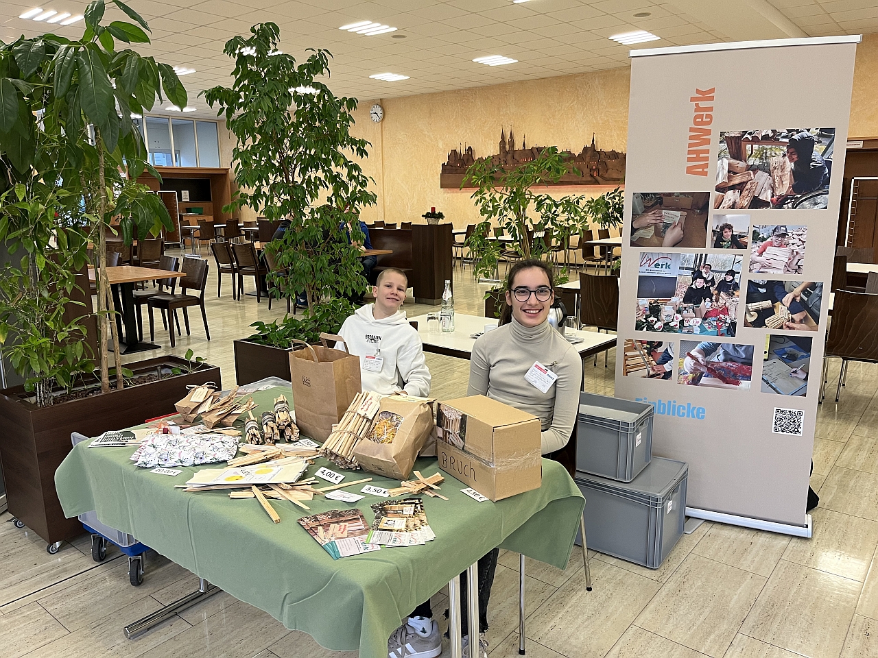 Zwei Schüler sitzen am Verkaufsstand, der in der Kantine der Firma Mahle steht. Auf dem Standtisch liegen Waren die in der Schule produziert wurden