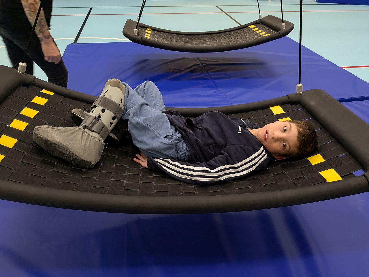 Ein Junge liegt in der Turnhalle auf einer großen Netzschaukel und schaut in die Kamera.