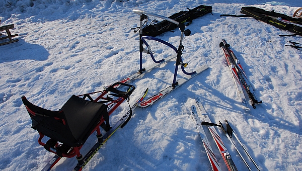 Im Schnee liegen verschiedene Ski und Skistöcke. Ebenso sieht man einen Skilator und einen Skisschlitten