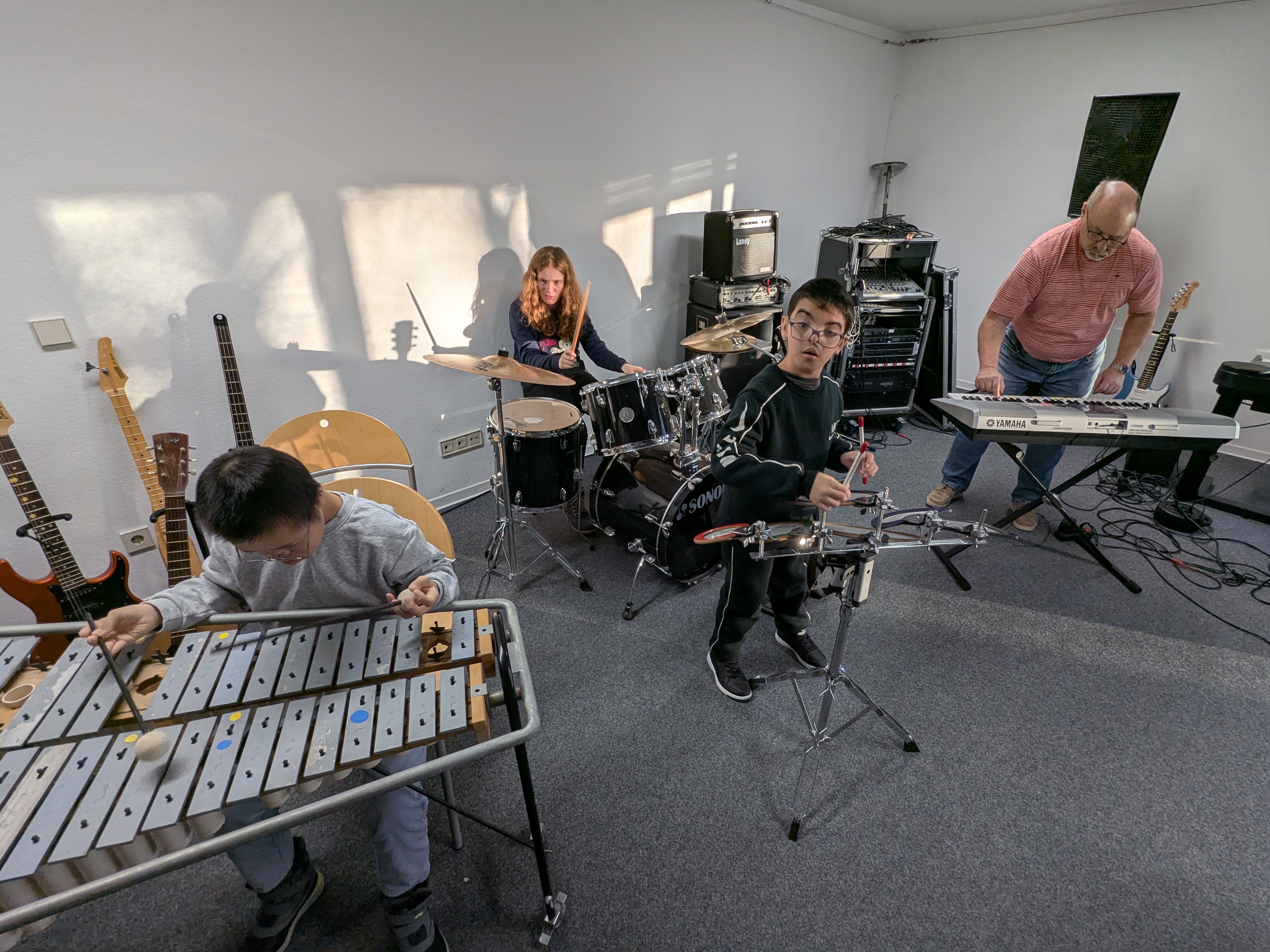 Eine Junge spiel ein Glockenspiel, ein Mädchen am Keyboard, ein Junge am Schlagzeug, ein Mann am Keyboard