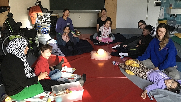 Die Schülerinnen und Schüler der Yoga-AG sitzen oder liegen im Kreis. Wir beginnen mit unserer Yoga-Zeit. Wir haben Besuch von Jara Alber. 