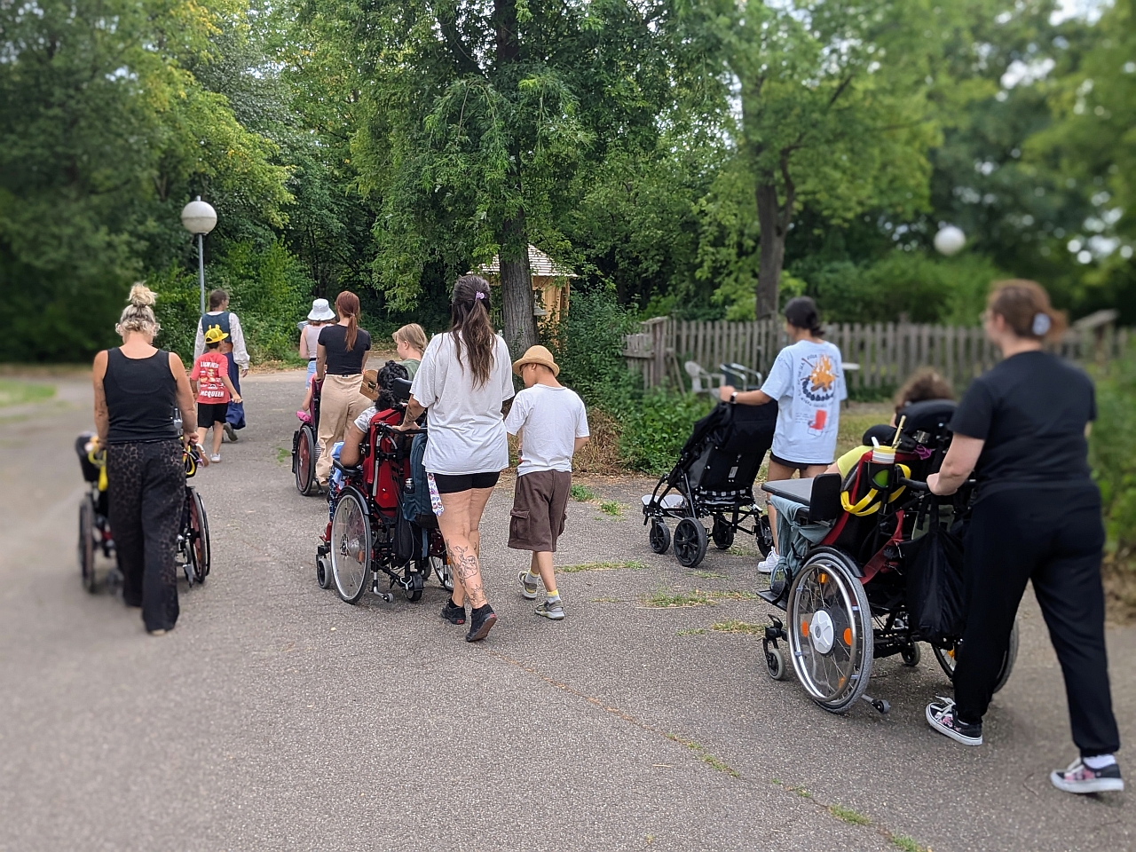 Eine Gruppe an Frauen und Kinder, teils im Rollstuhl laufen einen Weg entlang