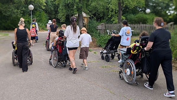 Eine Gruppe an Frauen und Kinder, teils im Rollstuhl laufen einen Weg entlang