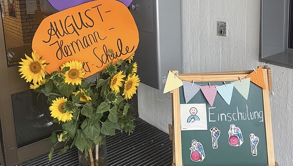 Begrüßung der neuen Erstklässler*innen durch gebastelte Schilder und Blumen vor dem Schuleingang. 