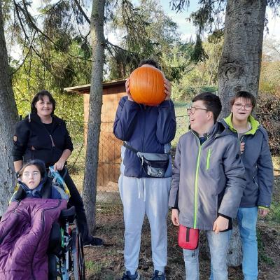 Vier Schüler und eine Mitarbeiterin freuen sich über einen gekauften Kürbis , im Hintergrund sind Bäume zusehen .