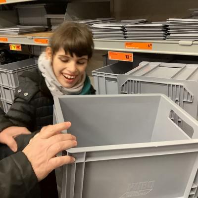 Anna trägt eine Box zum Wagen.