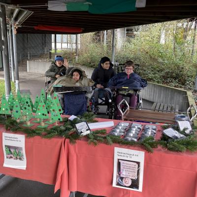 Die SchülerInnen stehen an ihrem Stand, an dem gebastelte Weihnachtsbäume angeboten werden. 