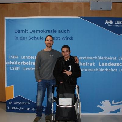 Herr Kling und Aziz stehen vor einer blauen Wand des LSK.