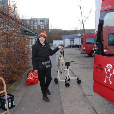 Julian trägt lachend eine Tasche zum Bus, der gerade eingeladen wird.