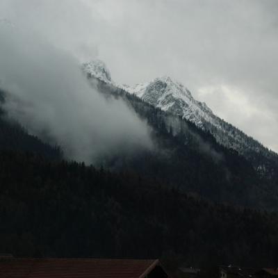 Man sieht eine Bergkette mit weißen Gipfeln. Der Himmel ist mit grauen Wolken verhangen.