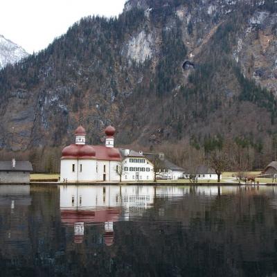 Vom See aus sieht man die Kirche von St. Bartholomä. Im Hintergrund sind Berge.