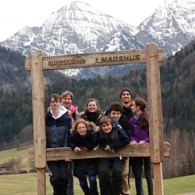 Vor einem schönen Bergpanorama steht ein hölzerner Rahmen. Darauf steht „Ruhpolding Madshus“. Im Rahmen stehen Florian Frau Gauch, Frau Fecke, Lara, Christopher, Julian, Herr Kling und Marija. Sie lächeln in die Kamera.