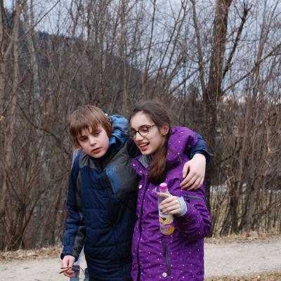 Christopher und Marija laufen neben einem Feldweg. Christopher hat den Arm um Marijas Schultern gelegt.