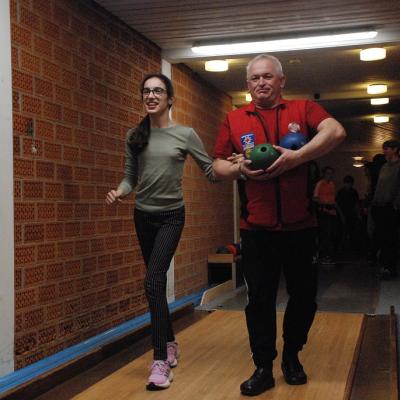 Marija wird von Martin von der Skiwacht zur Kegelbahn begleitet. Martin trägt zwei Kegelkugeln vor dem Bauch.