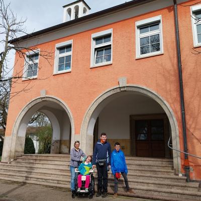 Im Hintergrund ist eine Kirche , vor der Treppe ist eine Rollstuhlfahrerin , zwei stehende Schüler und eine Betreuerin 