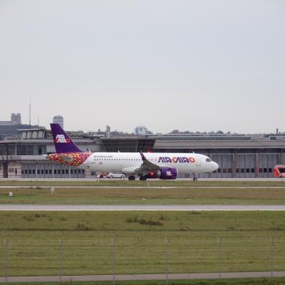 Auf einer Landebahn steht ein großes weißes Passagierflugzeug.  Es hat von der Airline Orange und Lila Schriftzüge. 