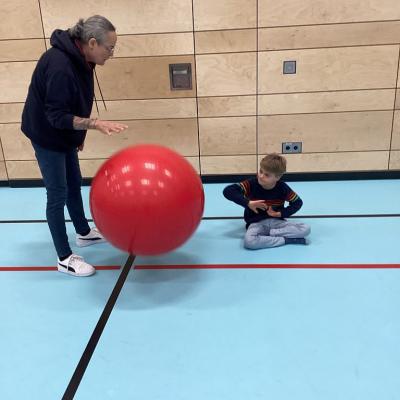 Eine Frau und ein Junge spielen mit einem großem rotem Pezziball.
