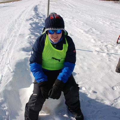Josua sitzt in voller Montur auf einem Schneehaufen und lächelt frontal in die Kamera.