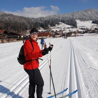 Frau Gauch steht auf der Loipe und dreht sich zur Kamera. Im Hintergrund sieht man ein großes Schneefeld und die schöne Landschaft mit dem guten Wetter.