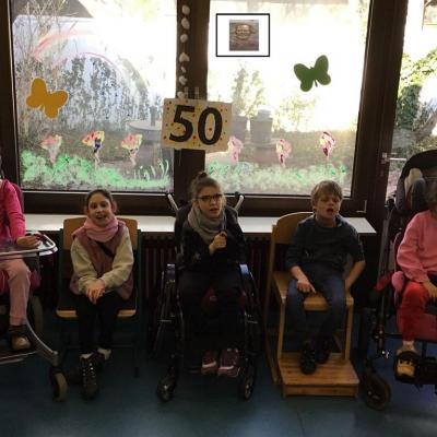 Das Foto zeigt von links nach rechts ein Mädchen im Rollstuhl, mit ernstem Gesicht, ein strahlend lächelndes Mädchen auf einem Stuhl sitzend, ein fröhliches Mädchen im Rollstuhl, einen Jungen auf einem Stuhl, ein Mädchen in einem Rehabuggy. 