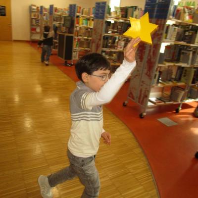 Ein Junge hält einen Papierstern in die Höhe. Im Hintergrund Regale der Stadtbücherei und ein weiterer Junge auf Suche.