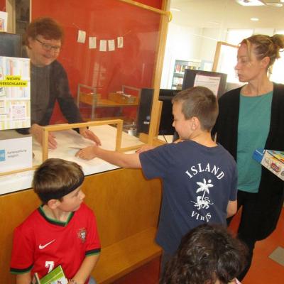 3 Kinder und ihre Lehrerin an der Ausleihe der Bücherei