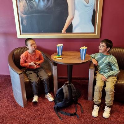 Zwei Jungen sitzen auf braunen Ledersesseln. Zwischen ihnen ein Tisch auf dem Popcorn steht. 