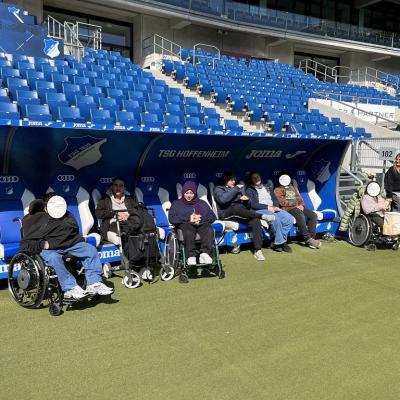 Auf diesem Bild sitzen fünf Schülerinnen und Schüler im Stadion. Sie sitzen auf der Auswechselbank der TSG Hoffenheim.