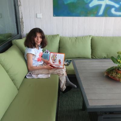 Ein Mädchen sitzt auf einem grünen Sofa auf einer Dachterrasse.