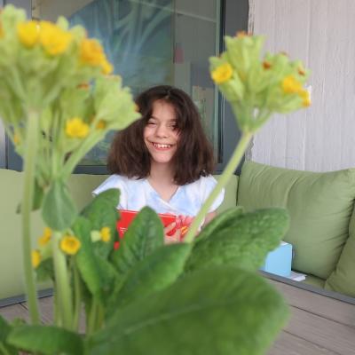 Ein Mädchen strahlt in die Kamera. Im Vordergrund sind Schlüsselblumen zu sehen.