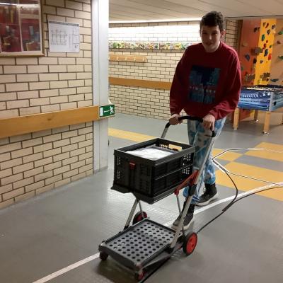 Julian schiebt einen Wagen mit Material.