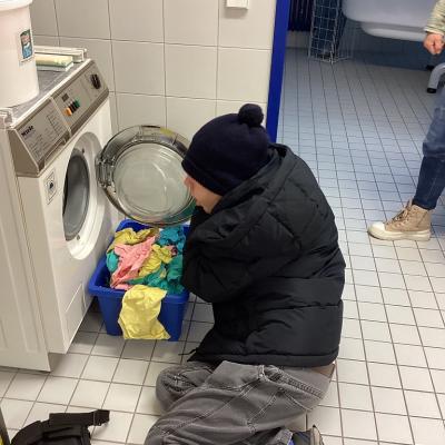 Joshua sitzt auf dem Boden und wirft Lappen in die Waschmaschine.