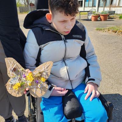 Schüler im Rollstuhl schaut den Schmetterling nicht an, der vor ihn gehalten wird , der Schmetterling ist sehr bunt voll mit Blumen